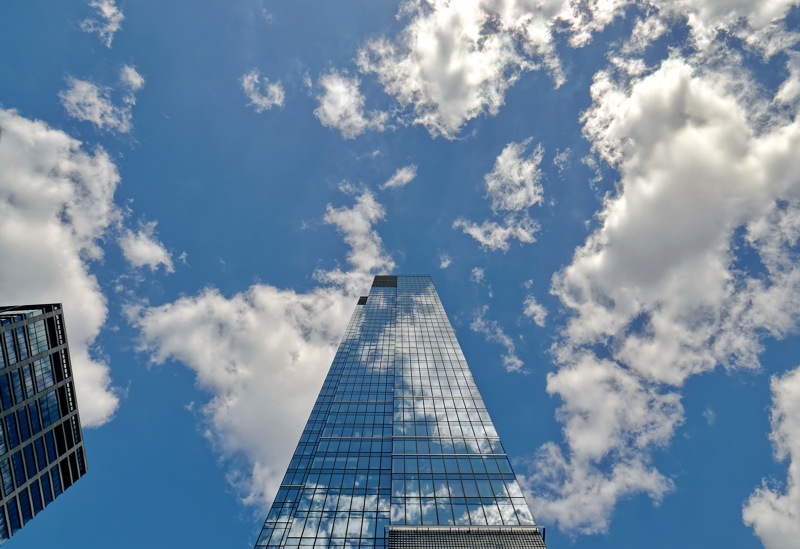 9 - A modern glass skyscraper in Warsaw with reflective facades mirroring a bright blue sky filled with white cumulus clouds